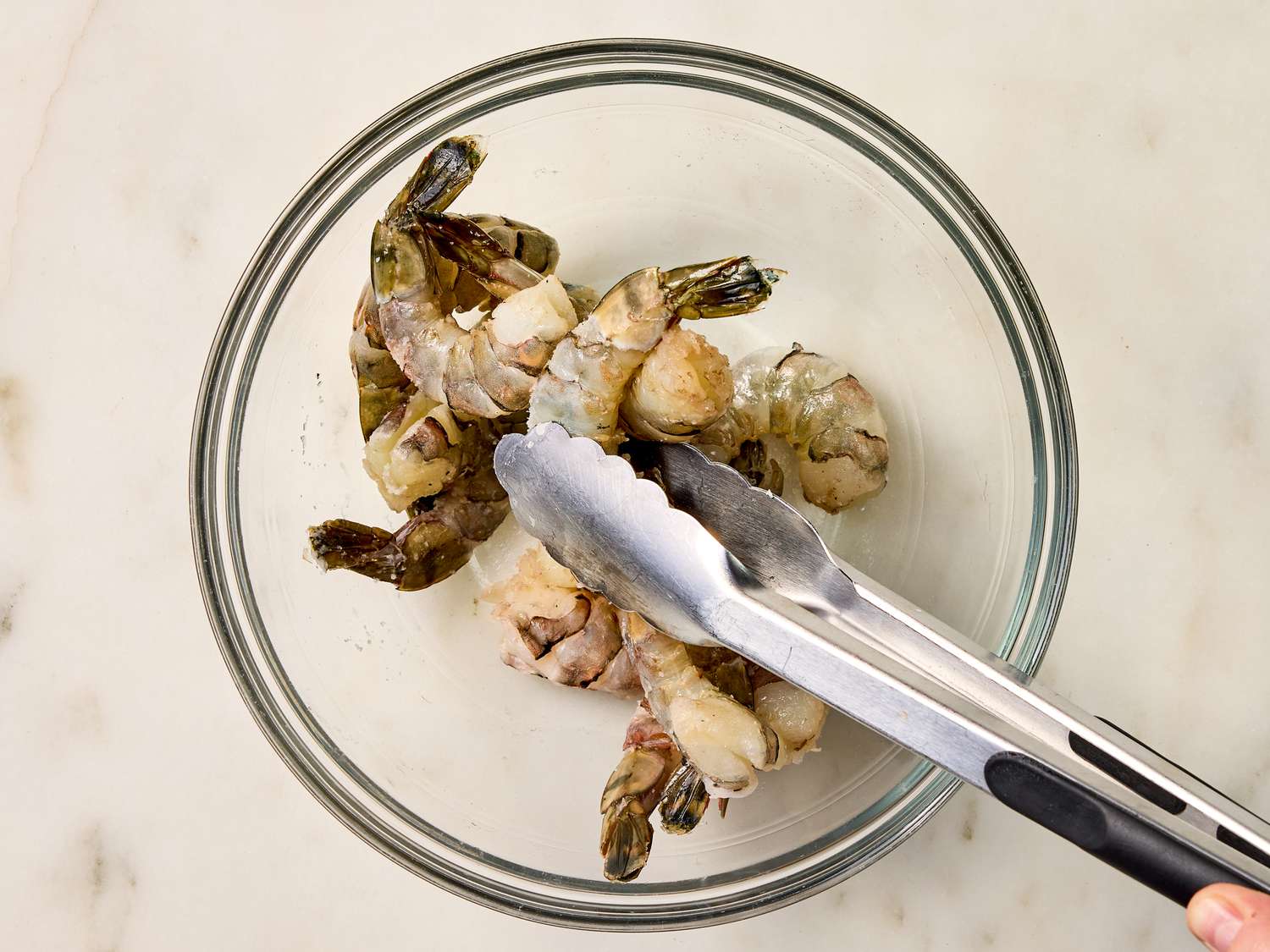 mixing shrimp with baking soda and salt with tongs i a glass bowl