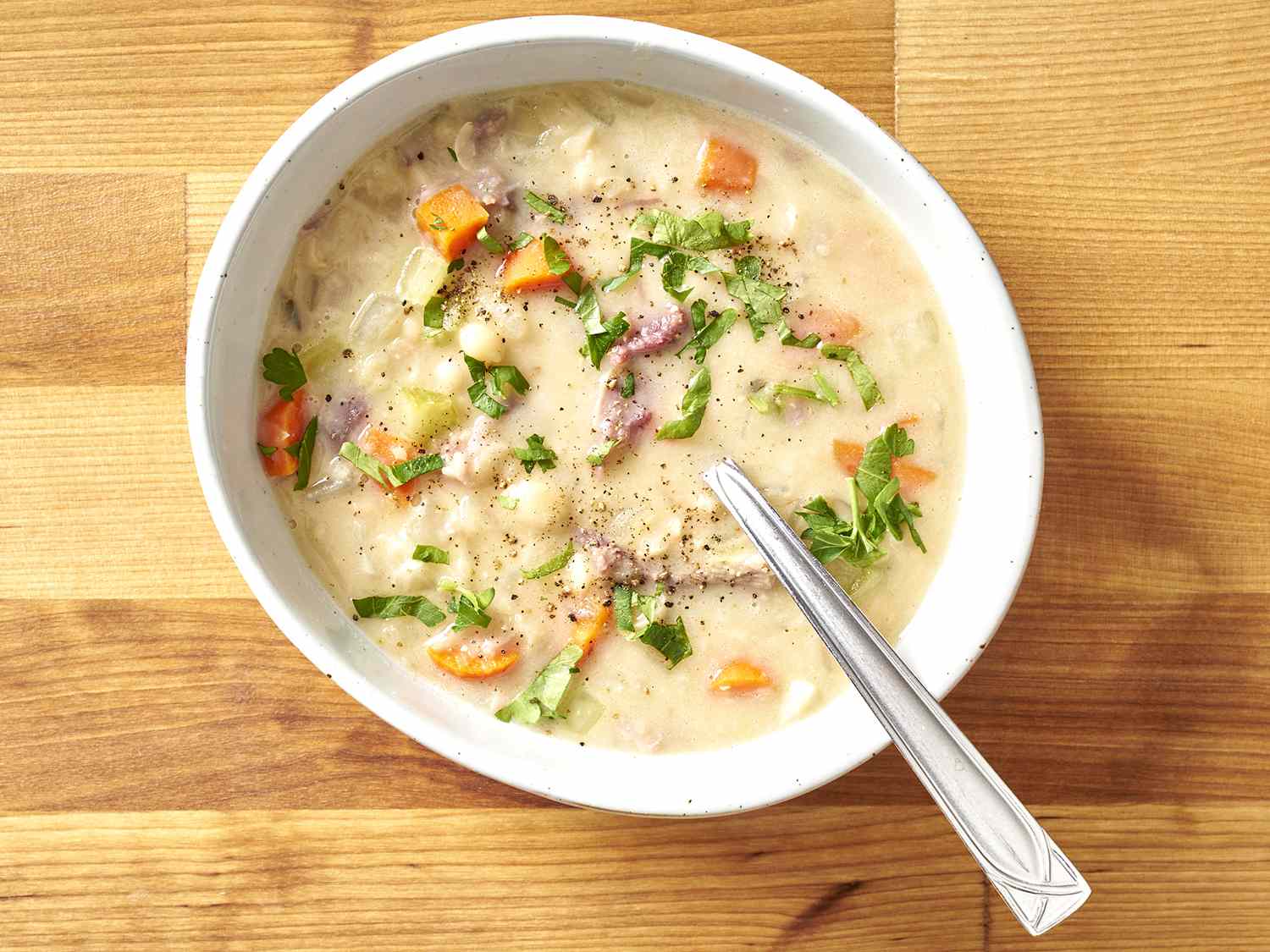 A bowl of ham & bean soup garnished with parsley.