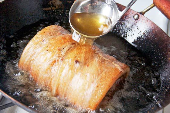 basting porchetta with hot frying oil in wok
