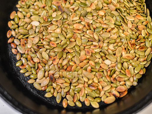Close overhead view of pepitas toasting in a cast iron skillet.