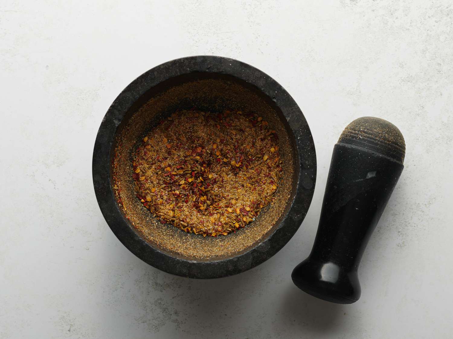 A stone mortar and pestle, with the mortar containing the pounded and ground spice mixture.