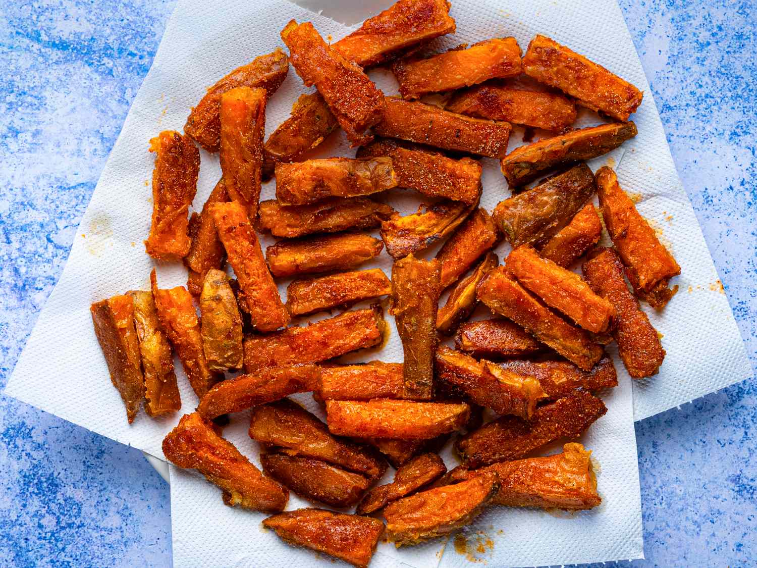 Sweet potato oven fries arranged on paper towels on a blue surface