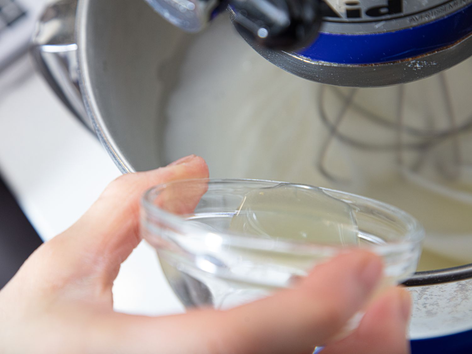 A person pouring a liquid ingredient into a stand mixer with a glass bowl