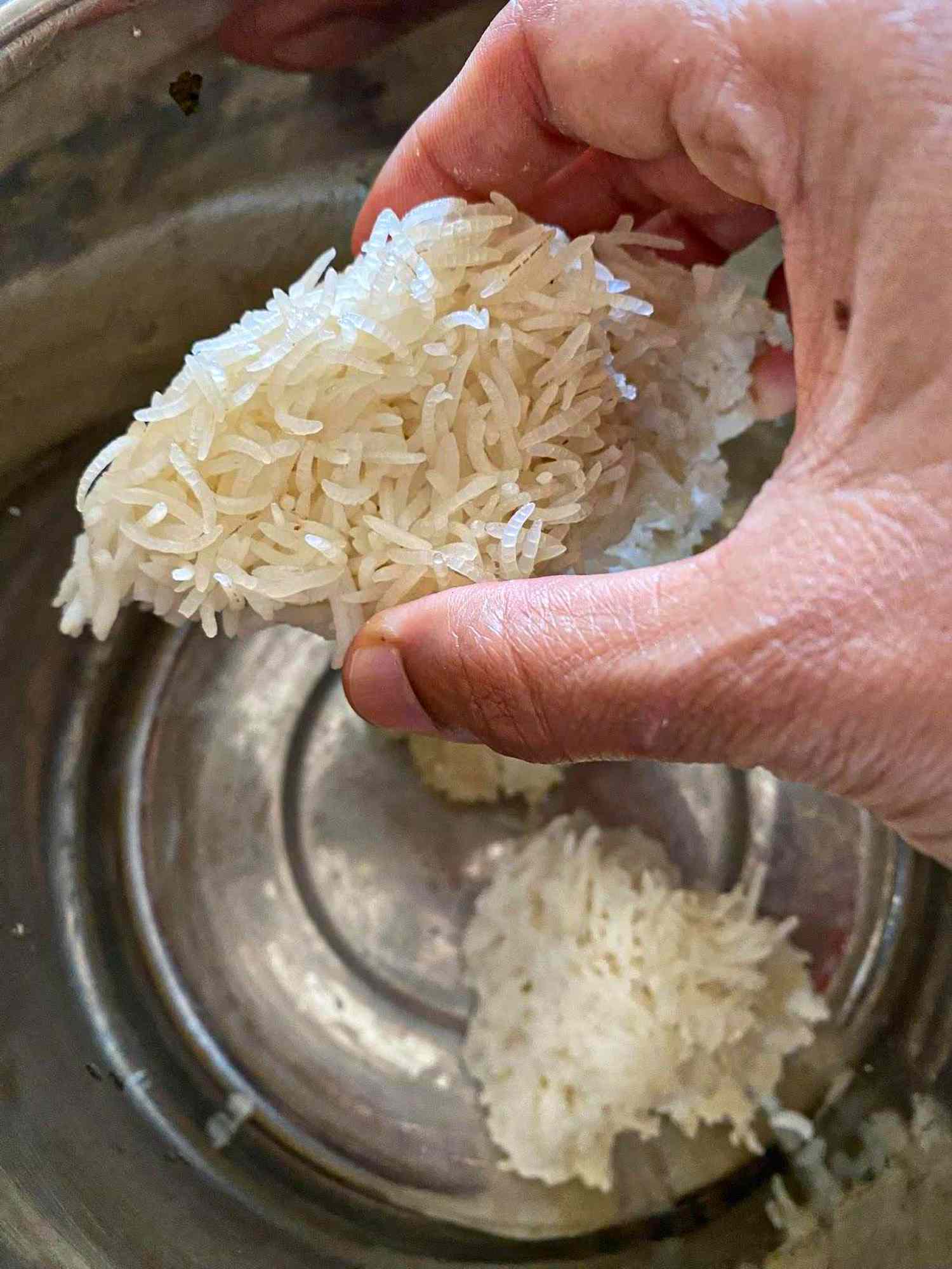 A person handling cooked rice in a pot using their hand