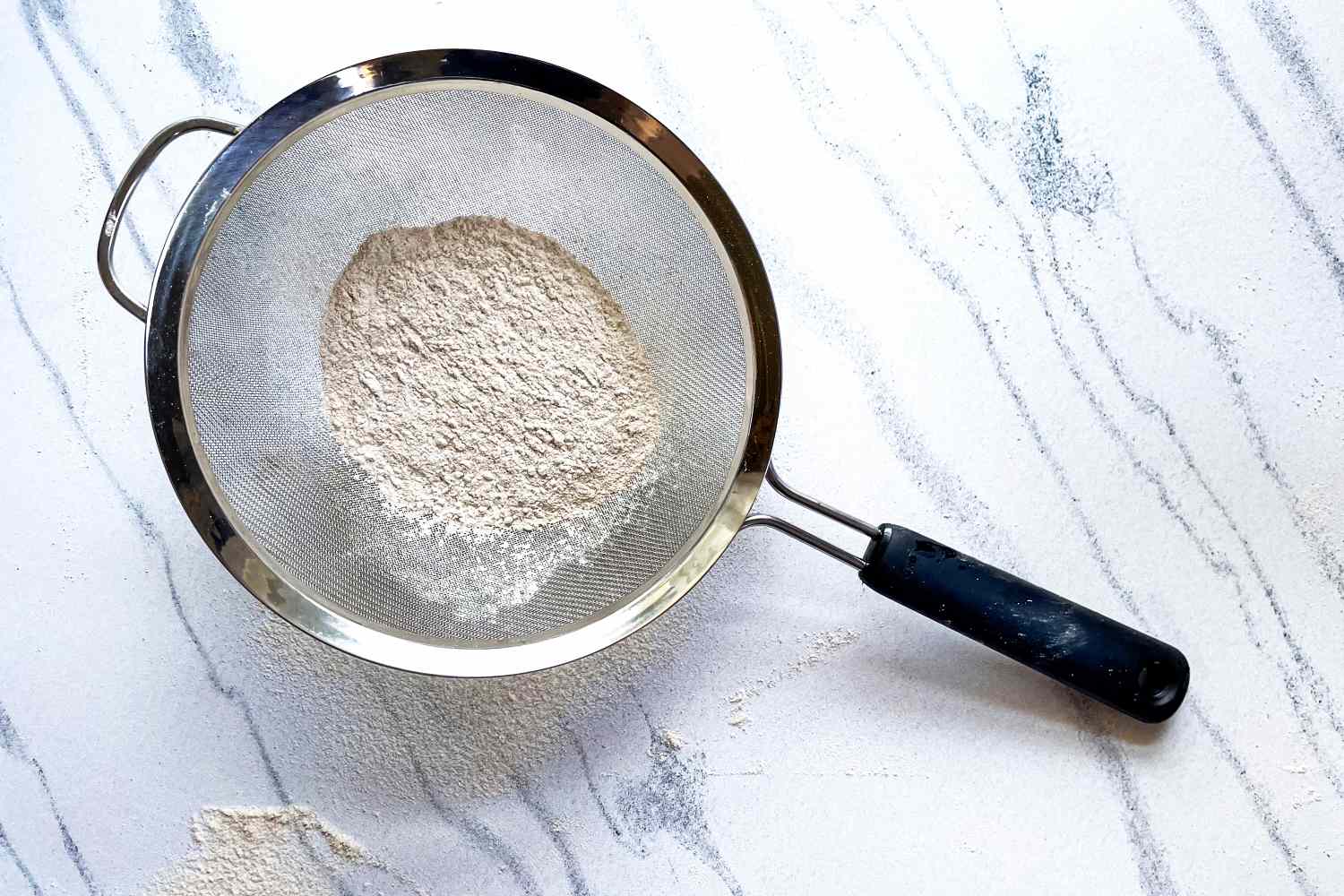 OXO Good Grips 8-Inch Double Rod Strainer with flour resting on a marble countertop