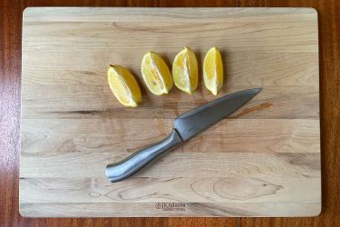 cutting board on counter with lemon wedges and knives