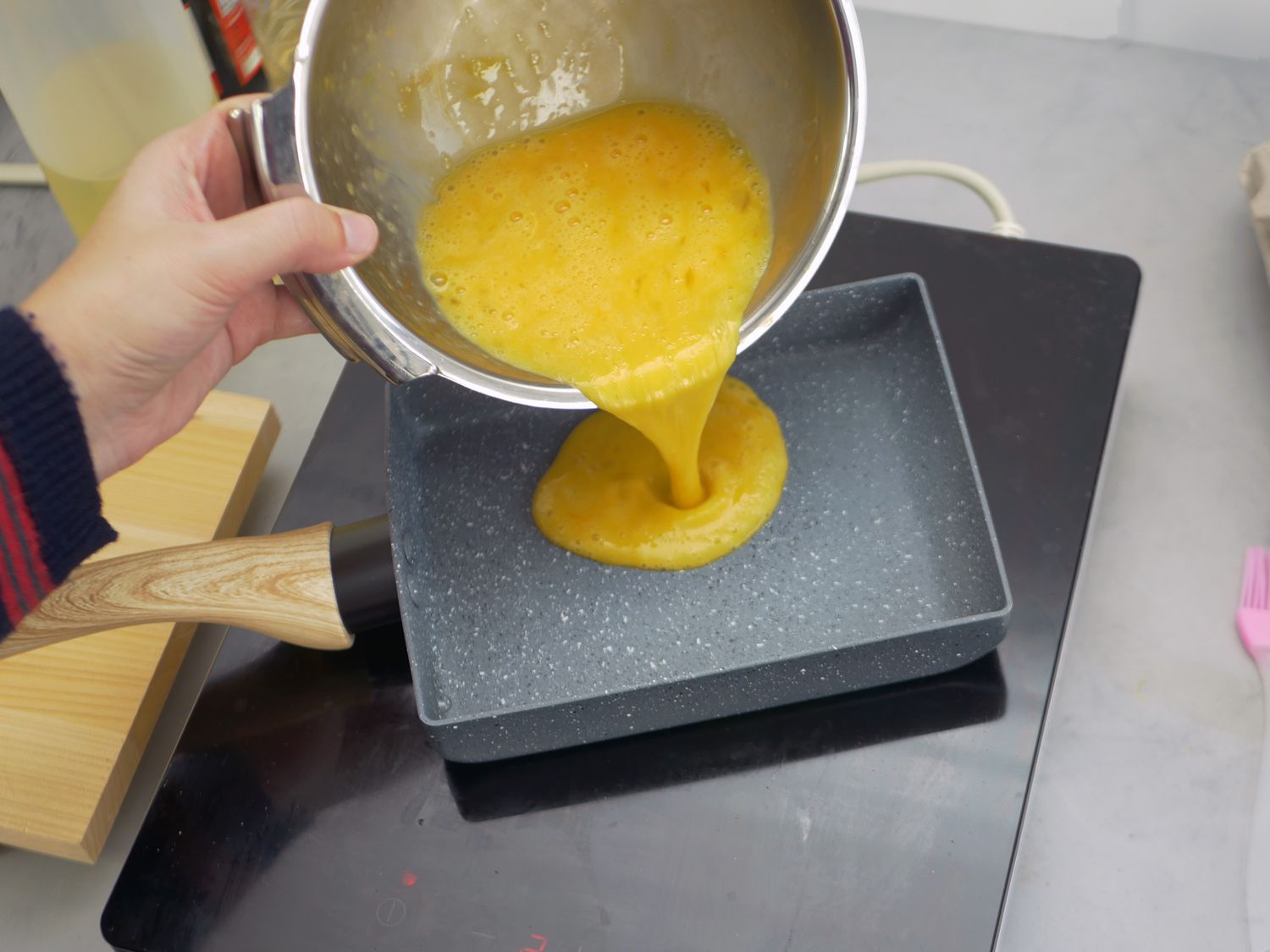 pouring egg mixture into a tamagoyaki pan on an induction burner