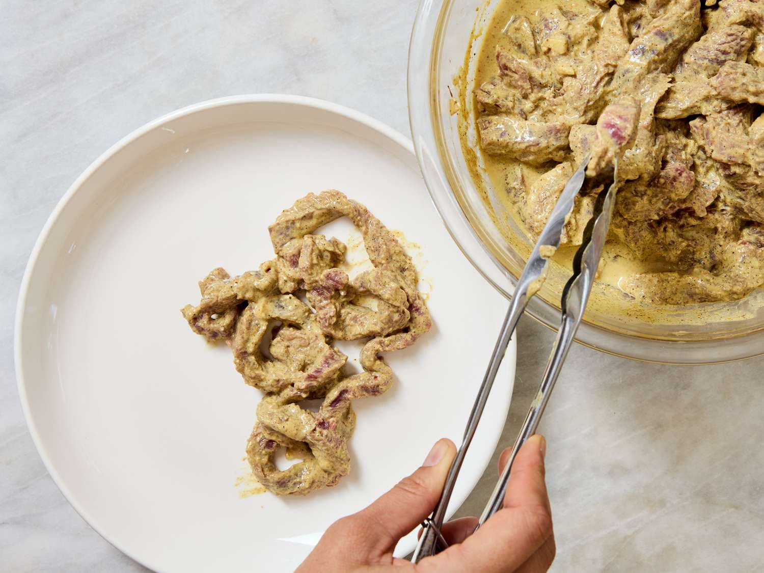 Preparation of beef shawarma raw marinated beef placed on a white plate using tongs
