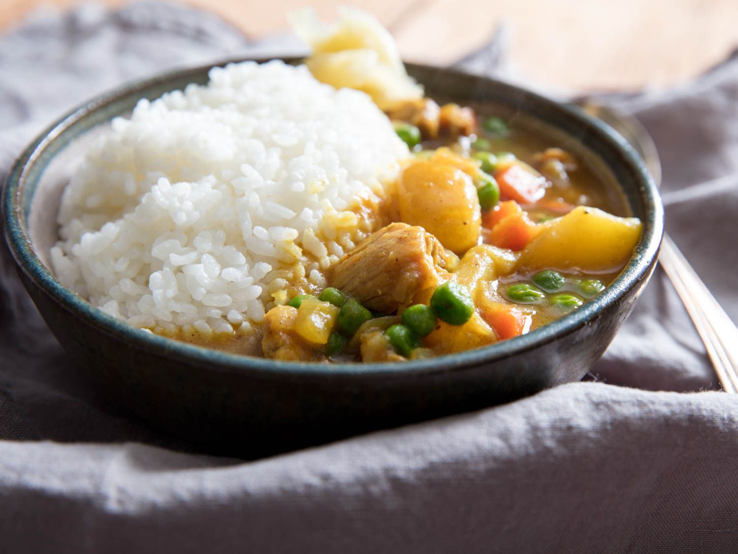 Japanese curry rice with chicken in a stoneware bowl on a lilac tablecloth.