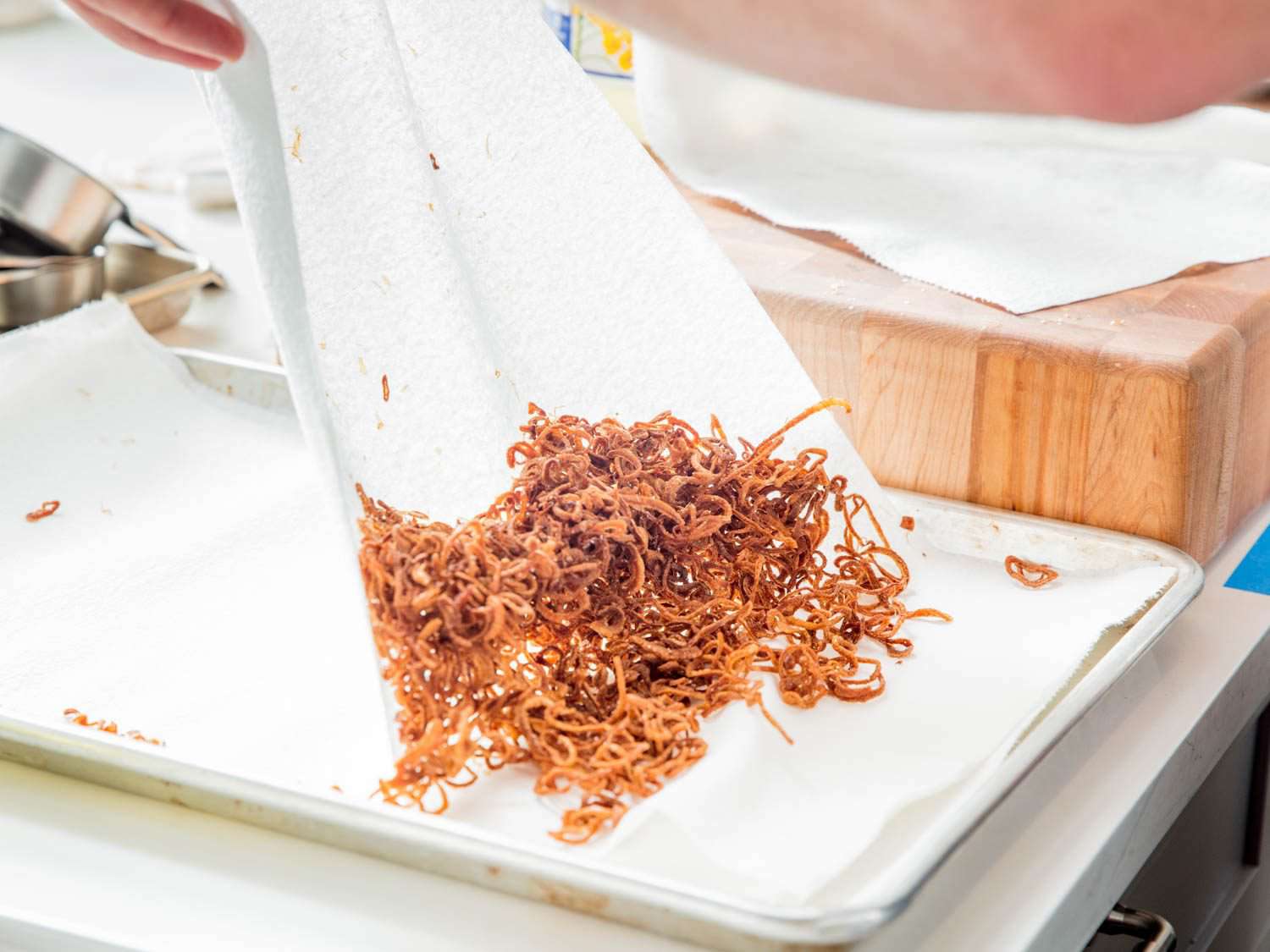 Pulling away a layer of paper towels so that the fried shallots don't get saturated in oil and remain crispy.