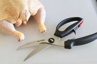 Poultry shears on a cutting board beside a whole chicken.