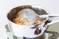 A stainless steel pot on a stovetop with a metal spoon stirring oatmeal