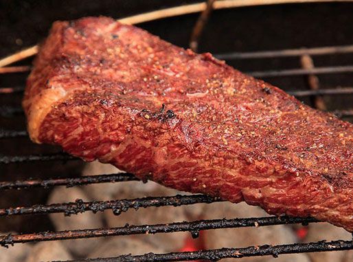 Close-up of a short rib steak on the grill. The steak has been turned to reveal the a browned, lightly charred crust. 