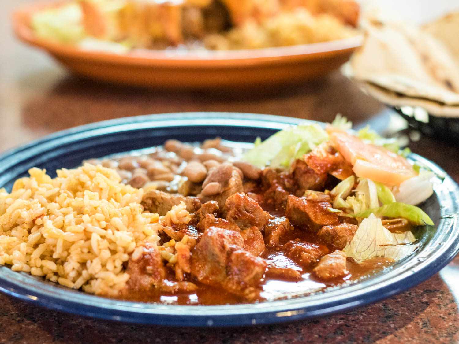 Carne adovada, served with rice, beans, and a pile of lettuce, onion, and tomato on a blue ceramic plate.