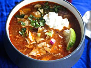 A bowl of slow-cooker chicken tortilla soup, topped with cilantro, avocado, sour cream, red onion, and lime.