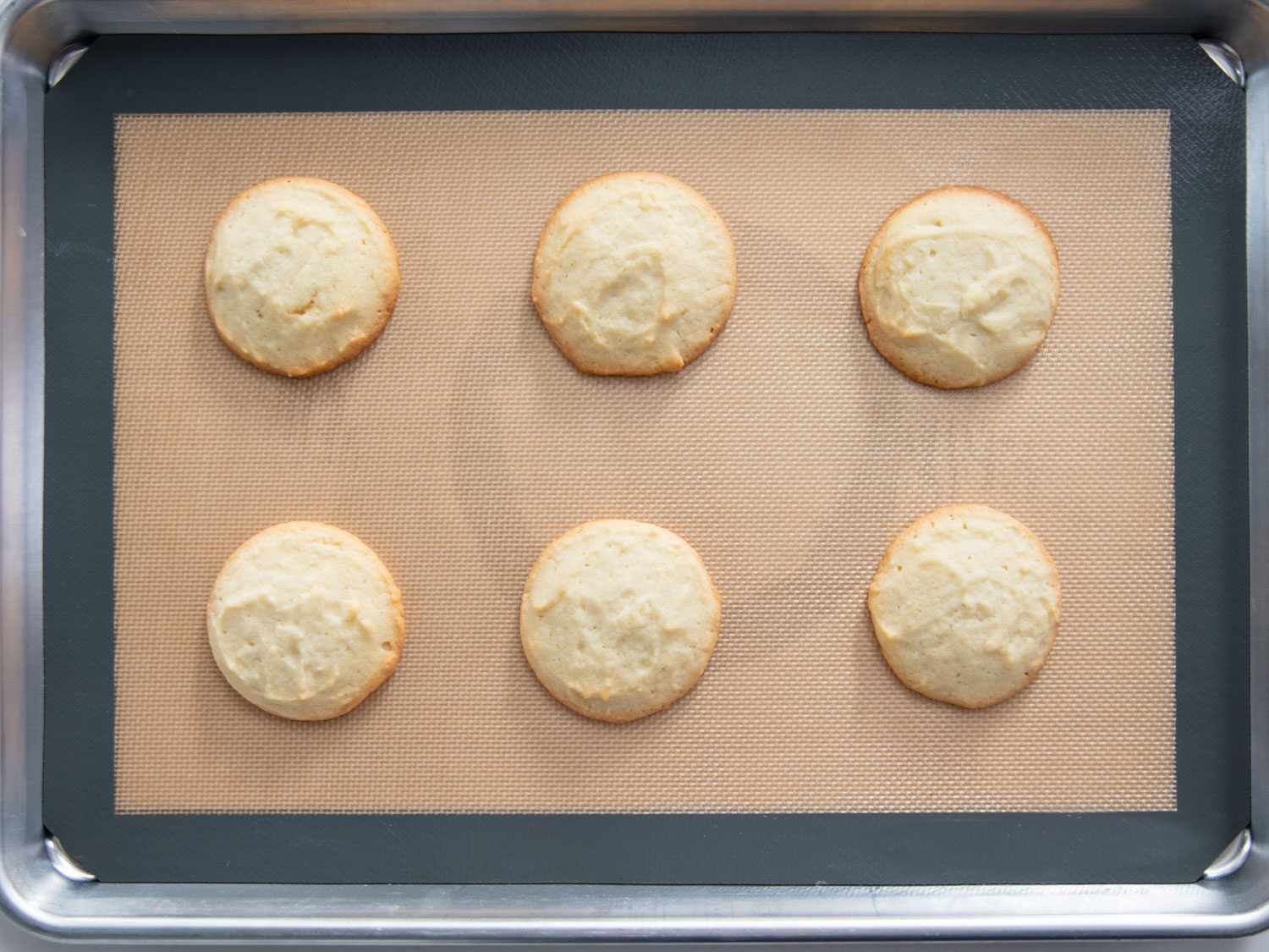 Overhead shot of unfrosted Lofthouse-style cookies, with excessive browning around the edges, baked on a silicone-lined baking sheet.