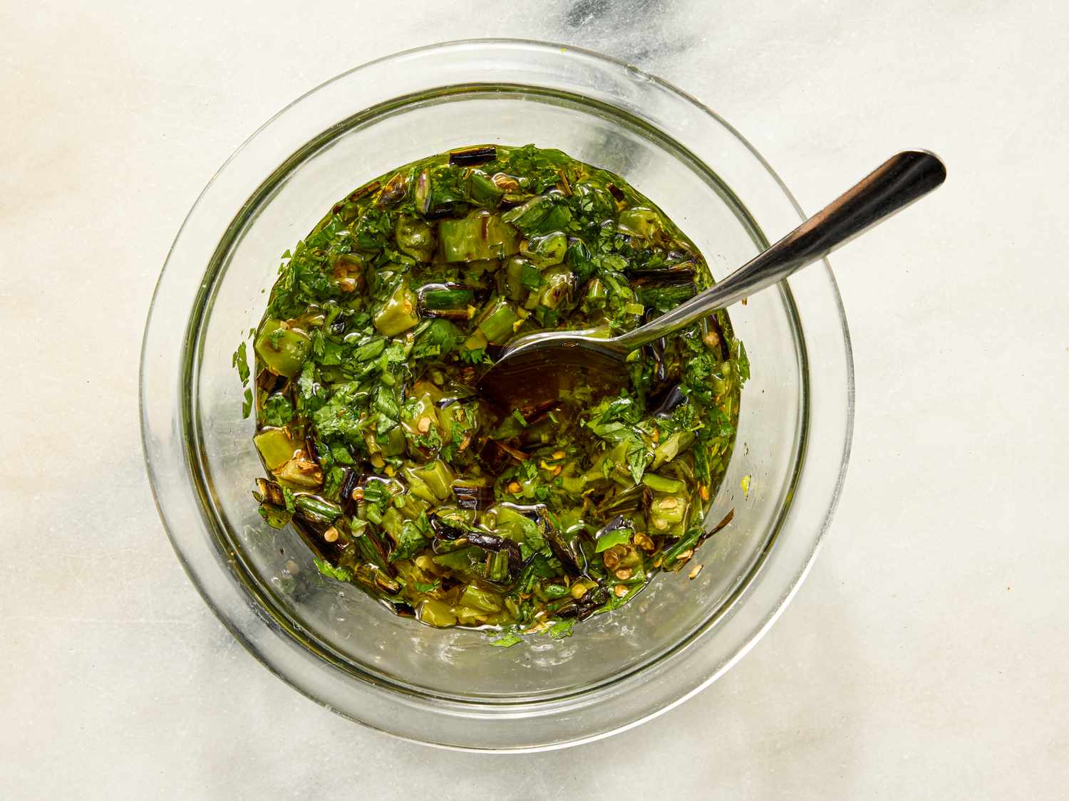 Glass bowl with a herb mixture and a spoon on a light surface