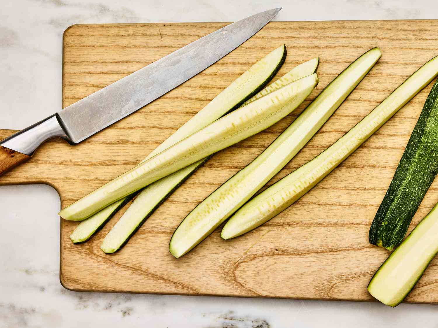 Zucchinis halved lengthwise on a cutting board, next to a knife 