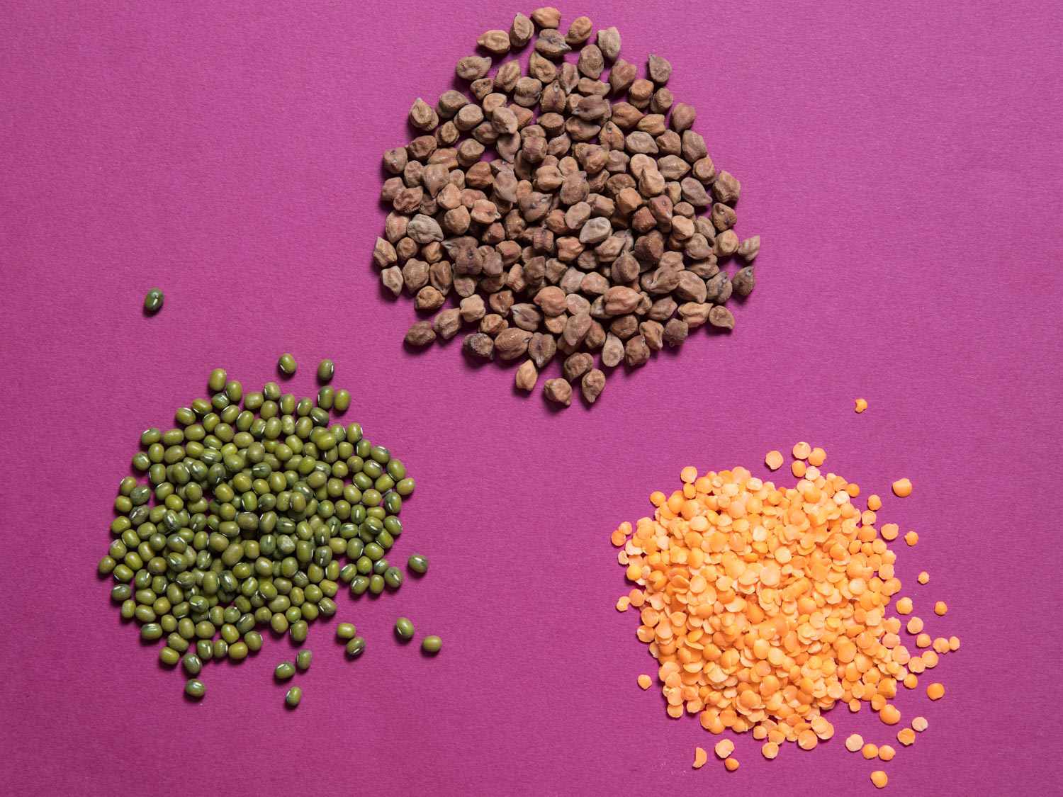 Overhead view of three types of dal, set on a fuchsia surface.