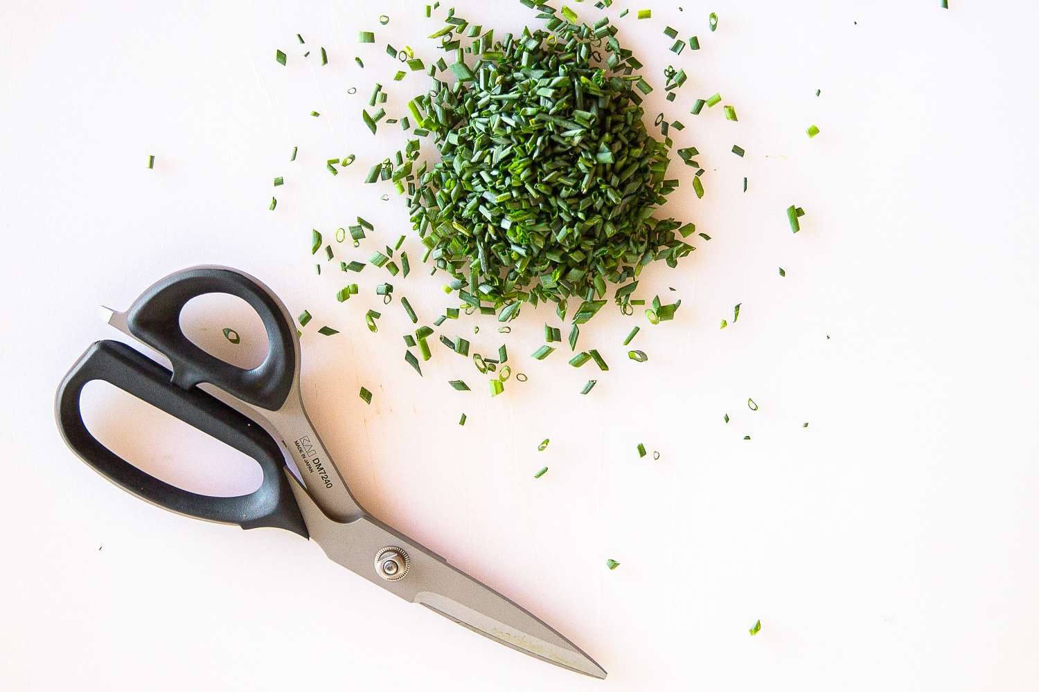 Shun scissors next to a pile of chopped green herbs on a white surface