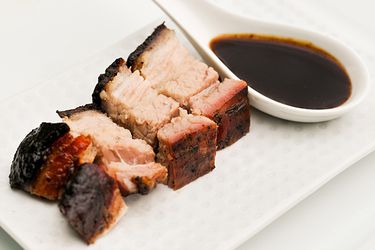 Char siu sauce in a spoon next to small cuts of cooked meat. 