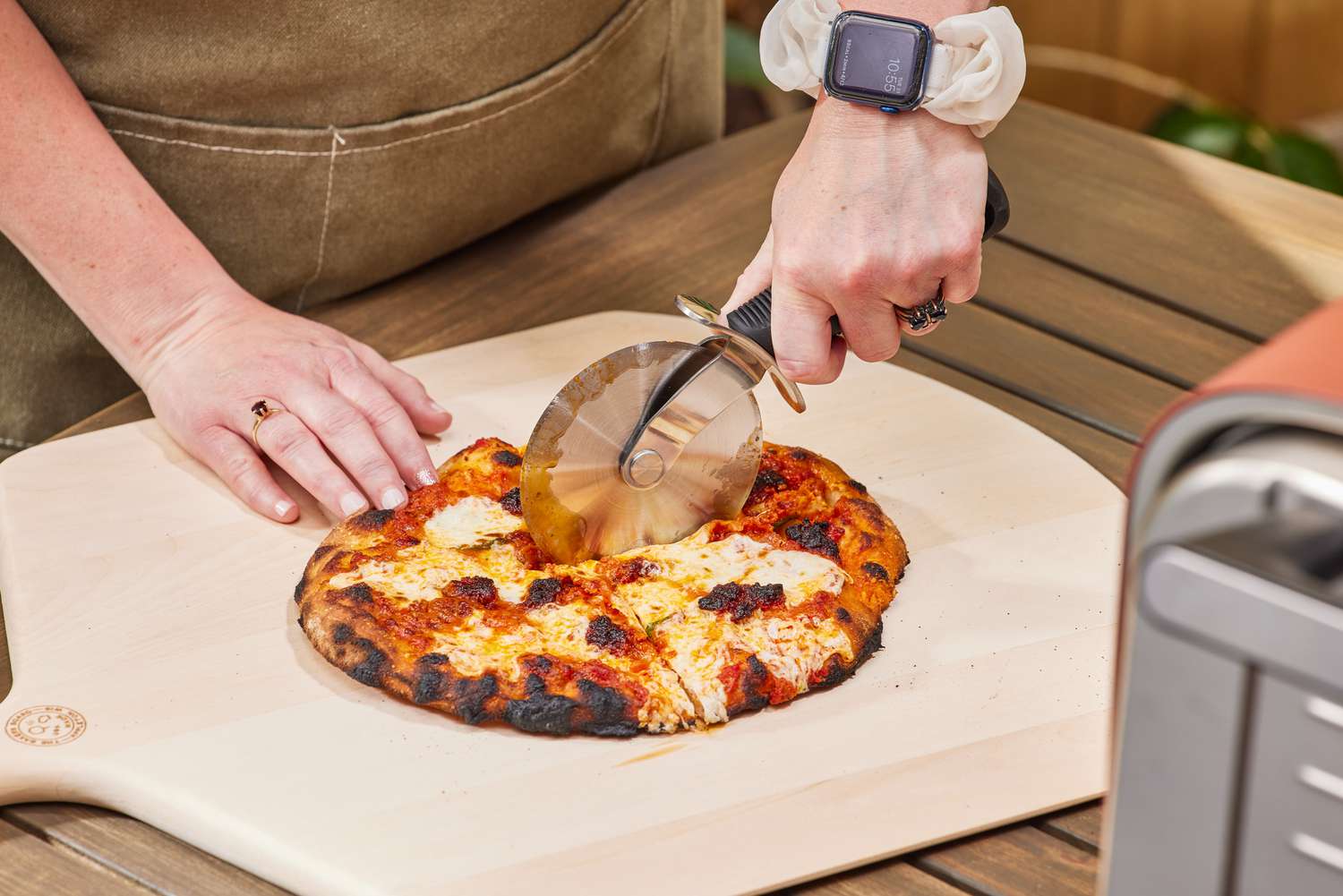 A person cutting a pizza made in the Ninja Woodfire 8-in-1 Outdoor Oven