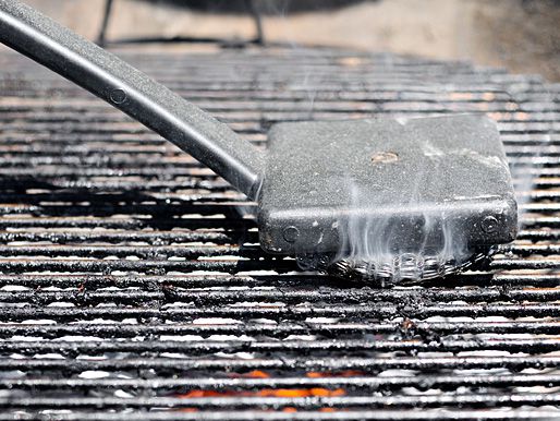 Using a grill brush to clean a hot grill grate.