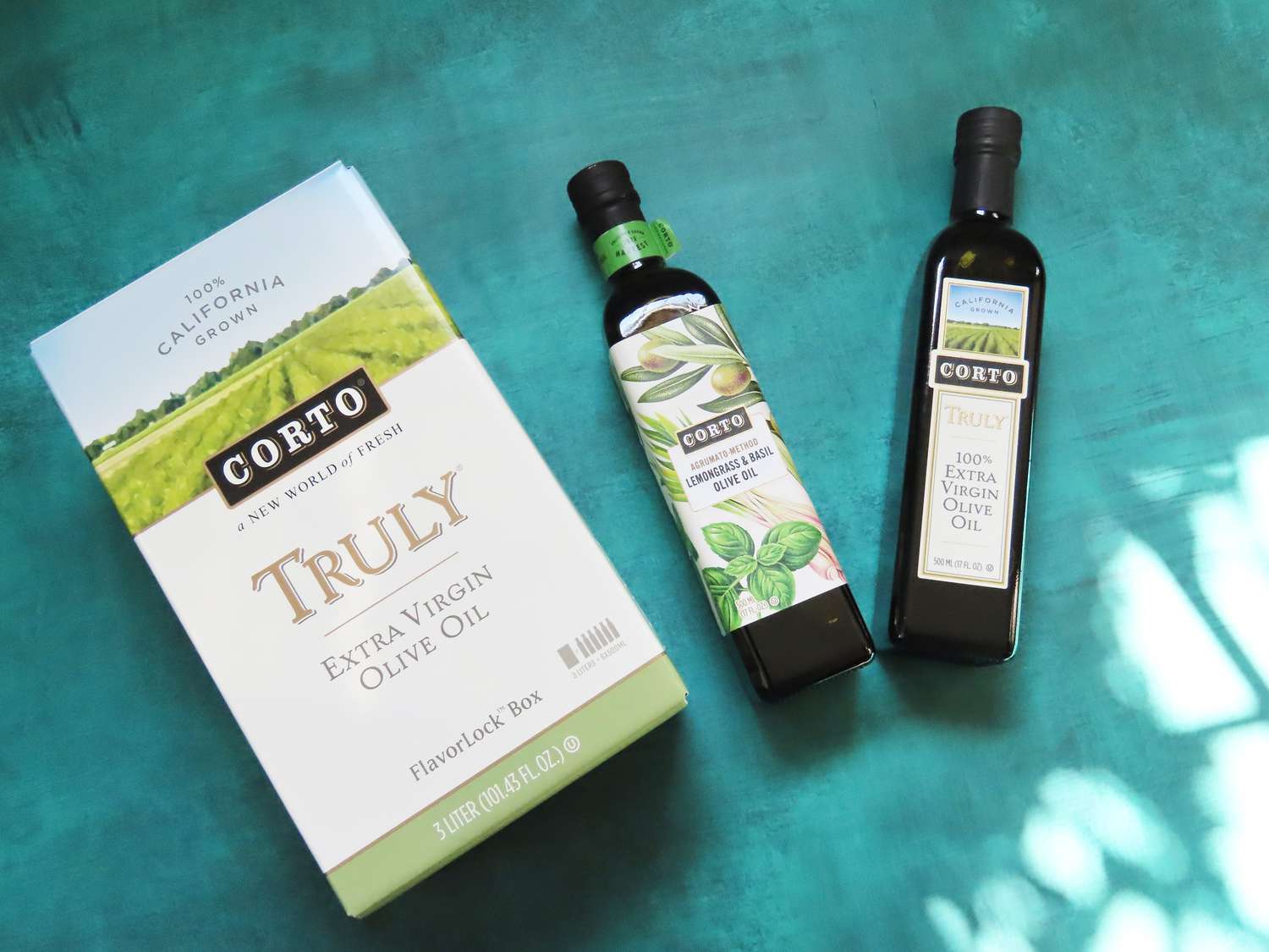 Two bottles of olive oil and one box of olive oil on a blue surface