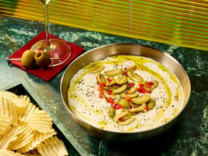 A dish of dip garnished with olives and crackers on the side