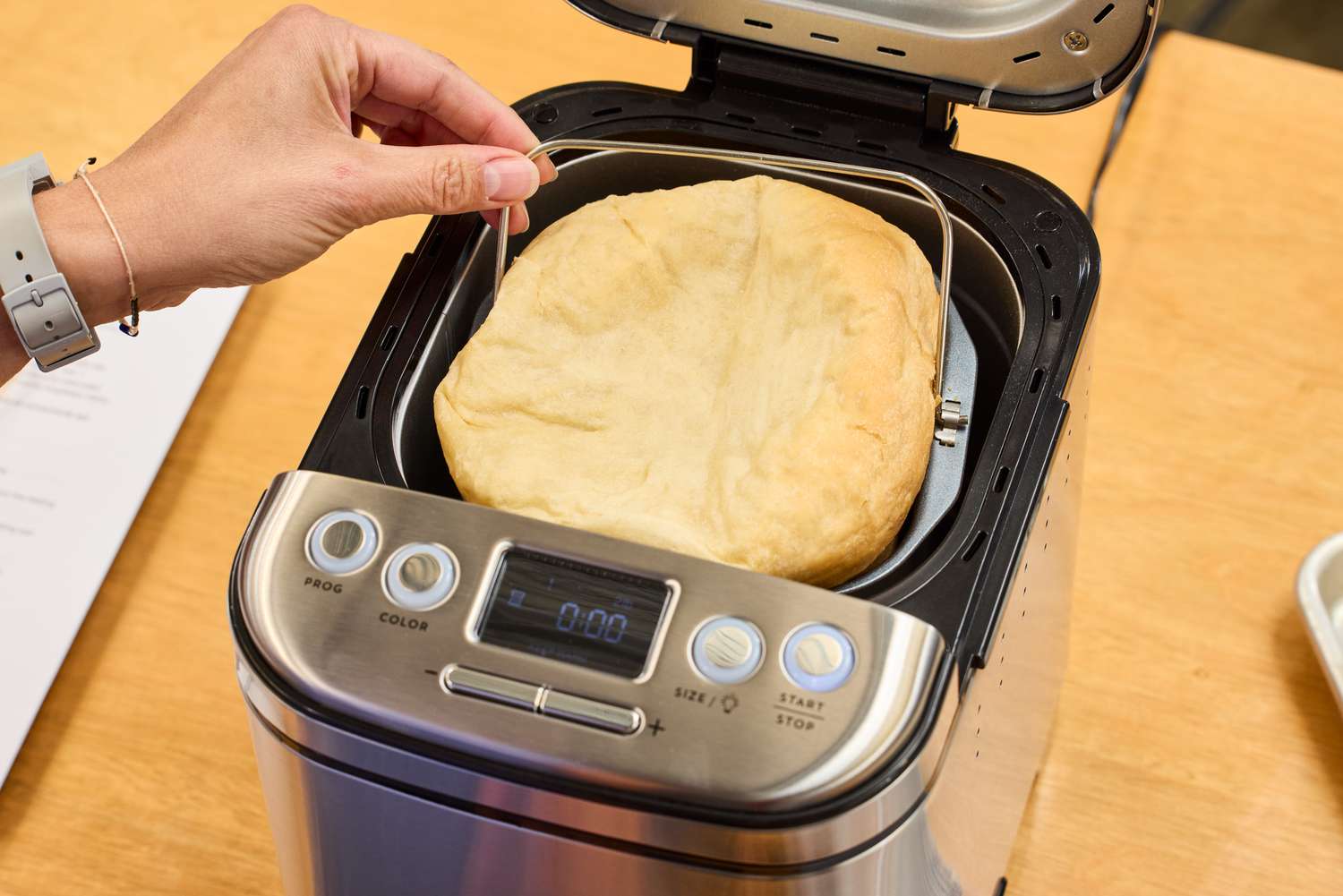 A hand removing the basket filled with bread from the Cuisinart CBK-110 Compact Automatic Bread Maker