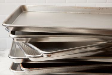 A stack of half-sheet pans in front of a gray tiled wall