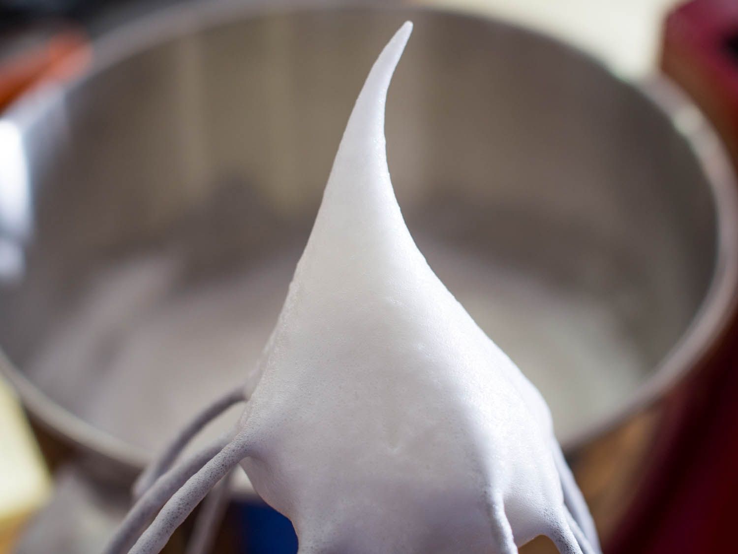 Beaten egg whites standing in a peak on the whisk of a mixer. 