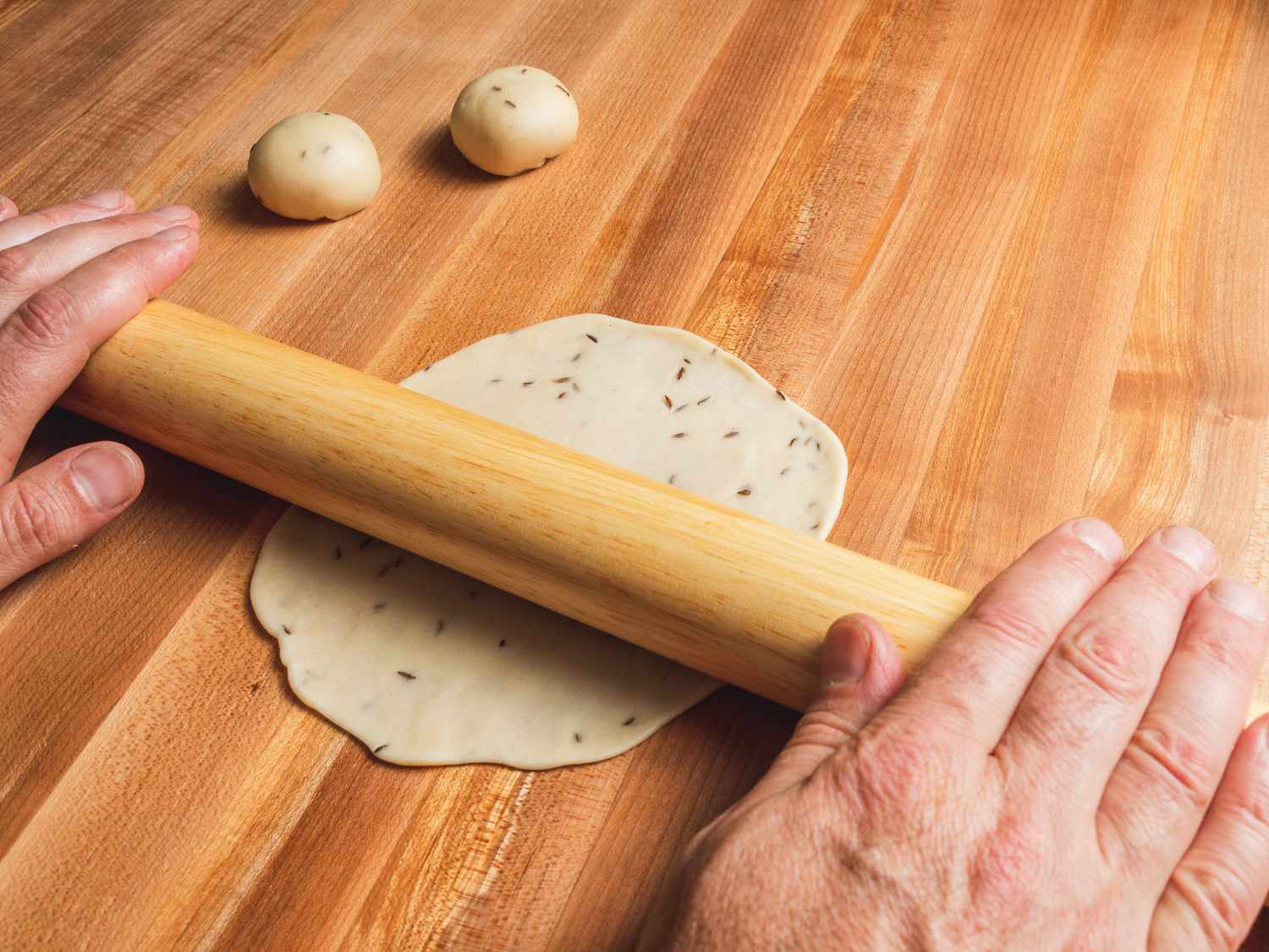 Samosa dough ball being rolled out with a rolling pin into a circle.