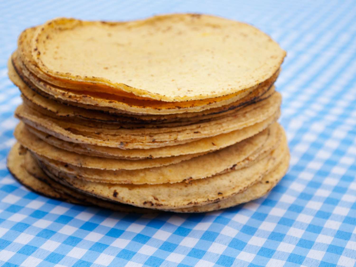 A stack of corn tortillas on a light blue checked tablecloth. 