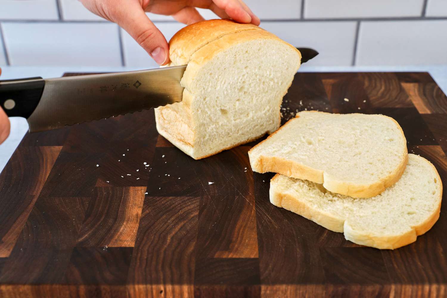 A hand slicing a loaf of bread with Tojiro F-687 Hand Made Bread Knife on a wooden cutting board
