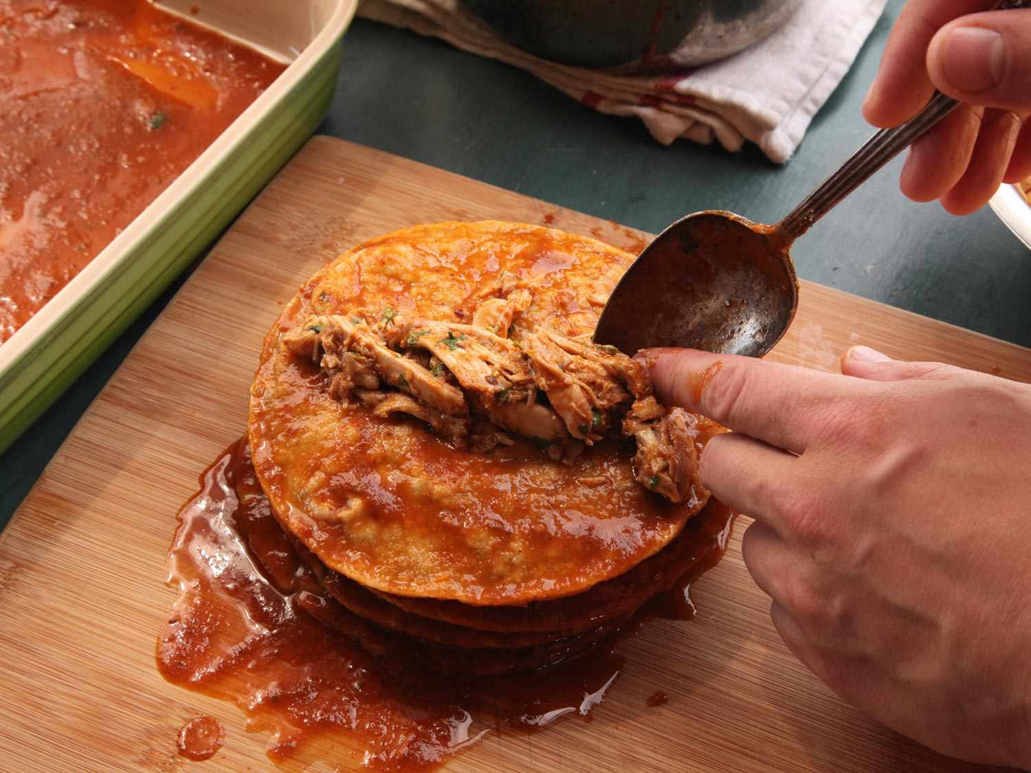 Arranging chicken filling in the middle of a sauce-soaked tortilla. 