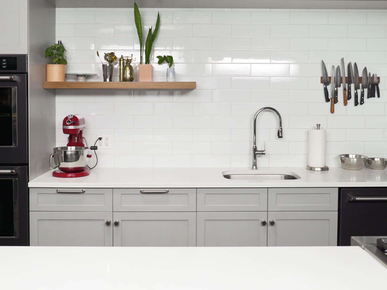 An empty Serious Eats test kitchen. The counters are white. On the counter against the wall, there is a red KitchenAid stand mixer on the left. On the right there are two mixing bowls next to a roll of kitchen towel and below a line-up of knives on the wall