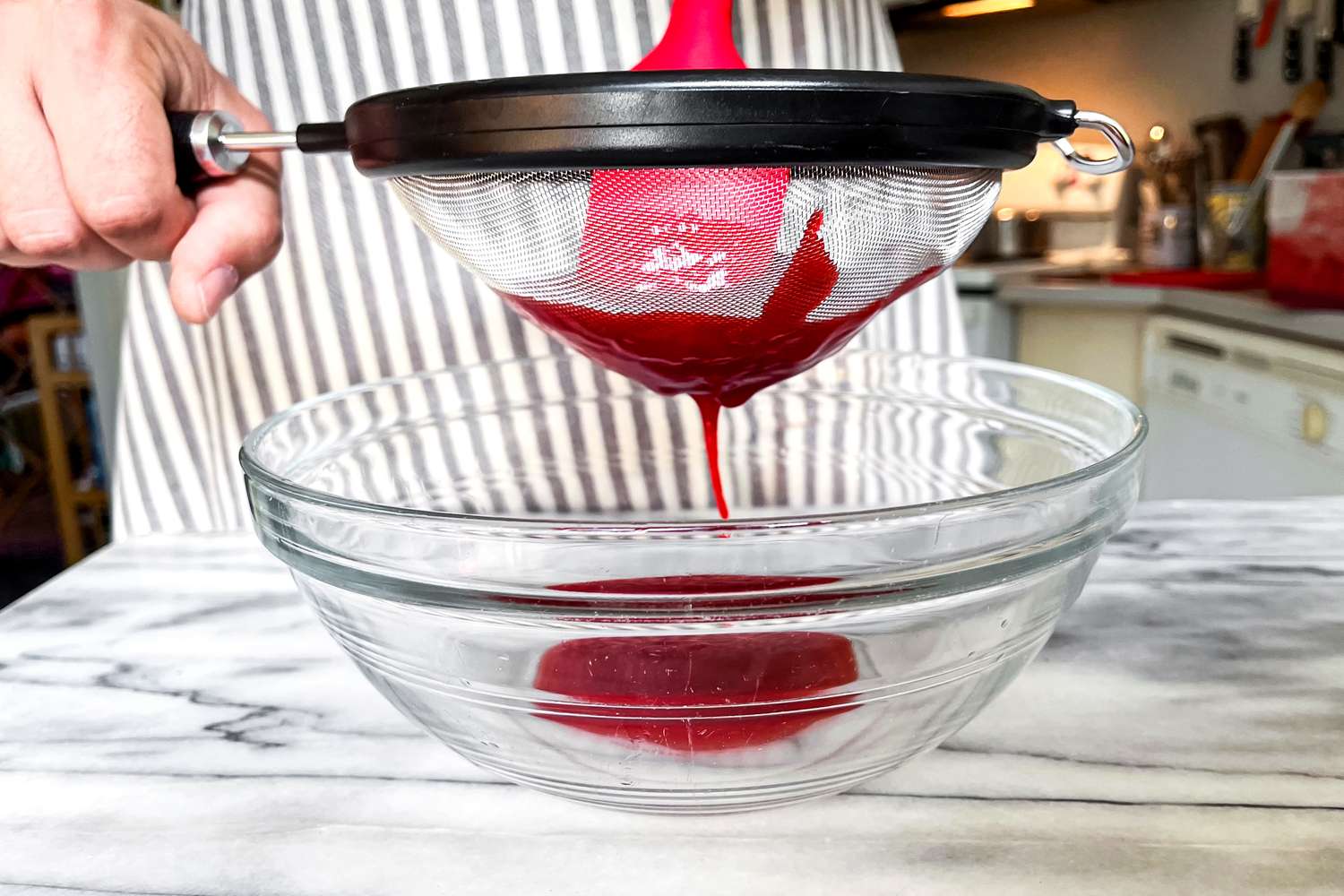 Person straining liquid through the KitchenAid Classic Strainer into a glass bowl
