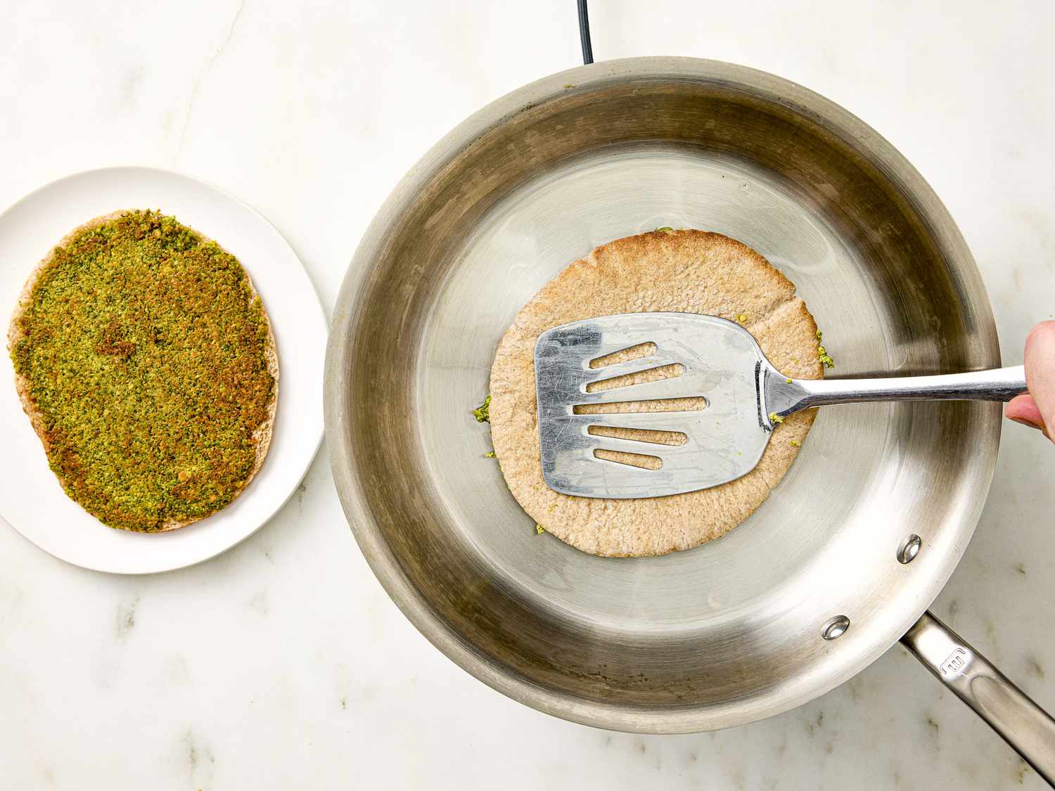 Falafel smash pita being cooked in a skillet, next to a plate with an already cooked falafel smash pita. 