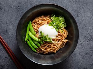 A bowl of mazemen ramen topped with an egg, snap peas, and sprouts