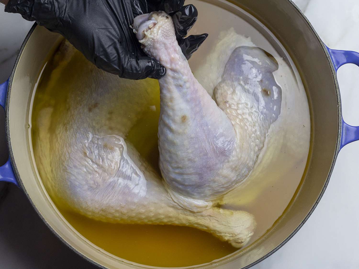 Turkey legs being submerged in one even layer into duck fat.