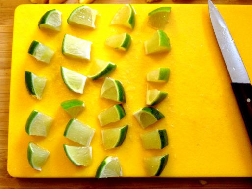 Lime wedges cut into smaller wedges on a cutting board.