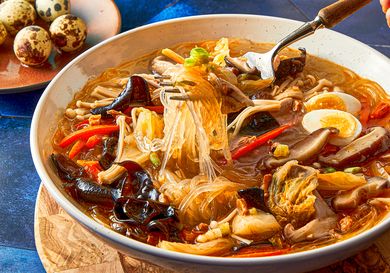 A bowl of sotanghon soup with vegetables quail eggs and mushrooms served alongside a plate of quail eggs