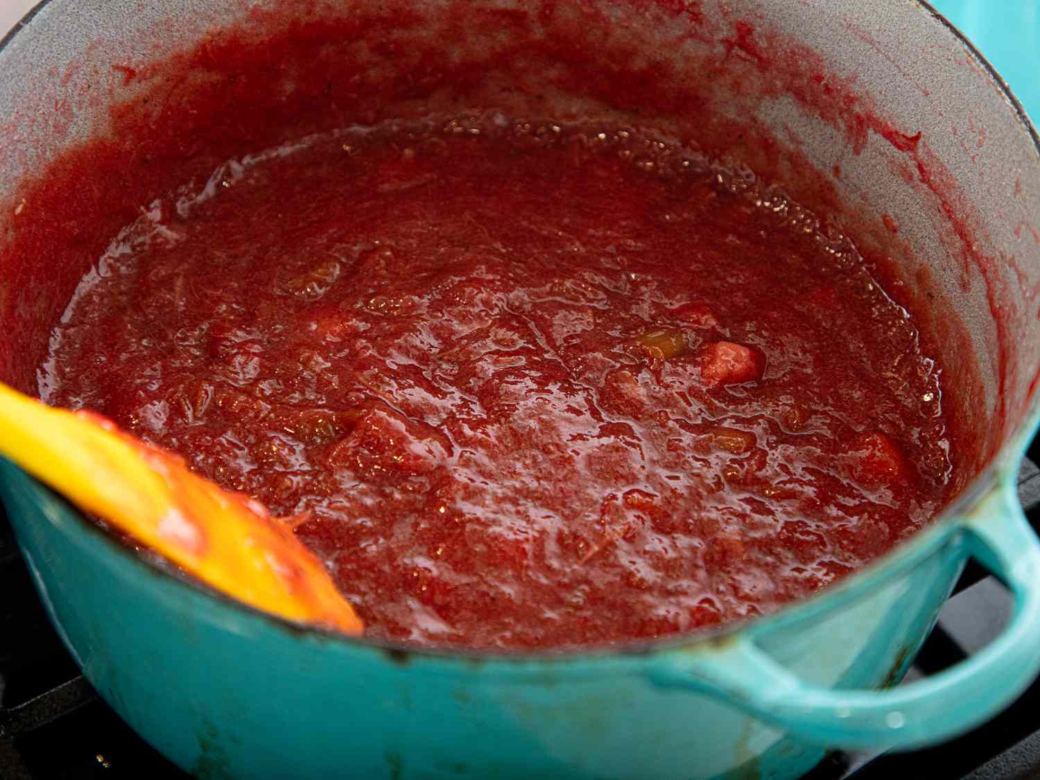 A pot of strawberry rhubarb jam being prepared, with a yellow spatula in the mixture