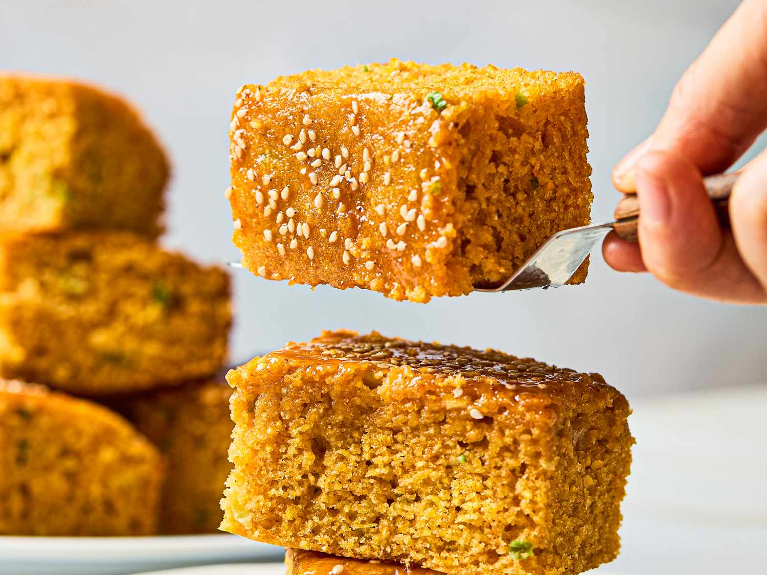 Stacked pieces of scallion cornbread with sesame topping one piece being lifted with a fork