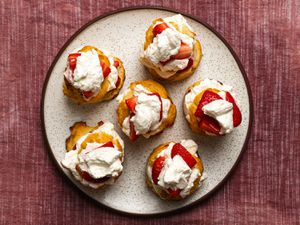 A top-down image of six composed strawberry shortcakes, on a speckled ceramic plate on a textured cloth background.