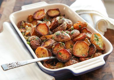 Casserole dish filled with roasted new potatoes with spoon sticking out.
