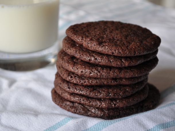 Stack of thin chocolate cookies next to glass of milk