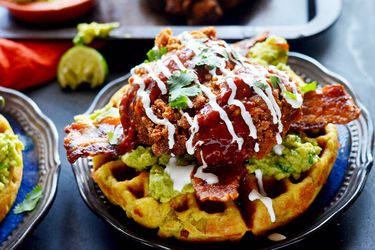 A plate of fully-loaded Mexican chicken and waffles on a blue plate. 