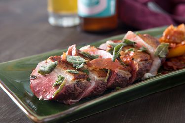 Sliced duck breast on a green rectangular platter, with a glass of sour beer in the background